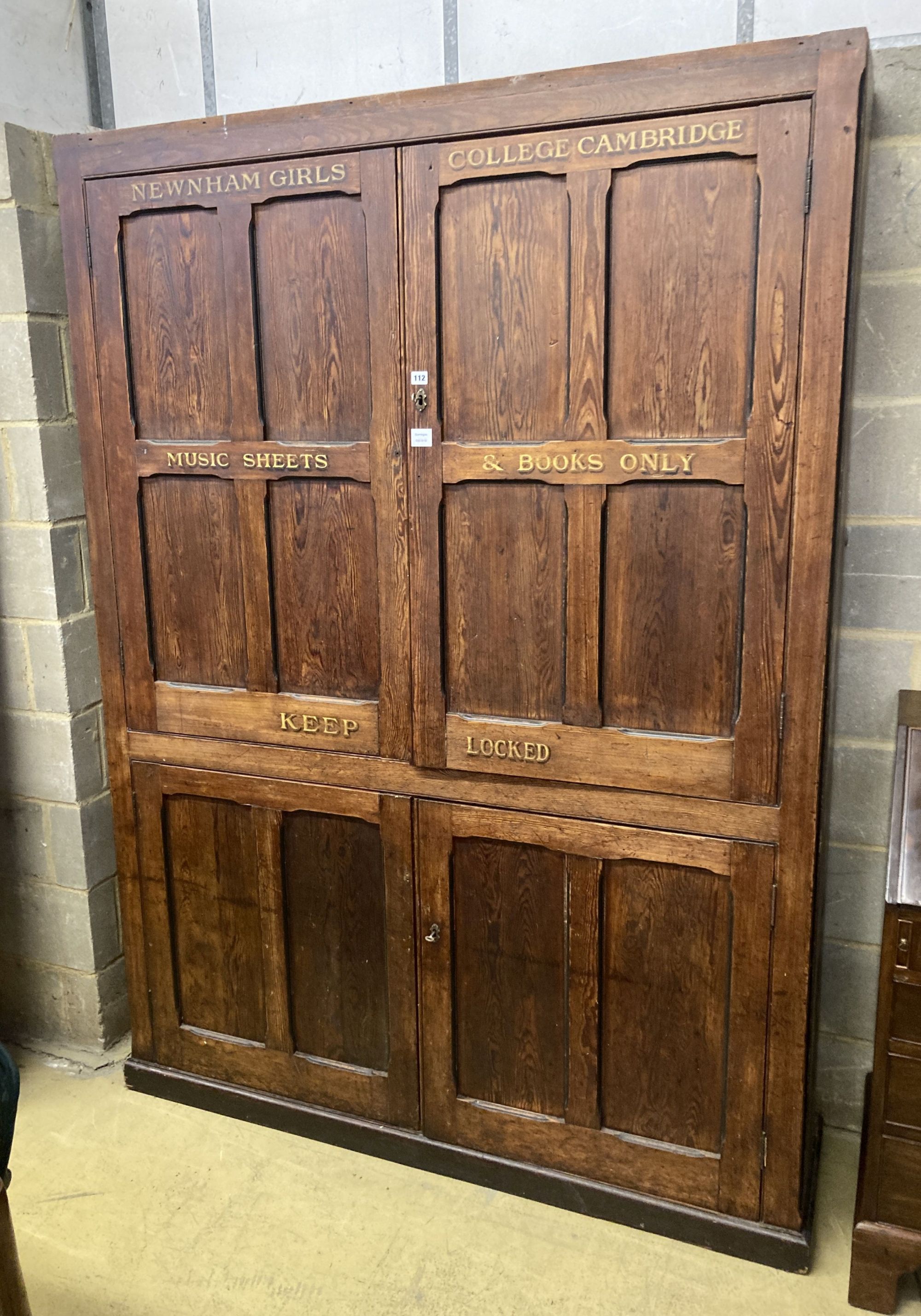 A Victorian panelled pitch pine four door cabinet, upper section marked in gilt, Newnham Girls College Cambridge music sheets and book